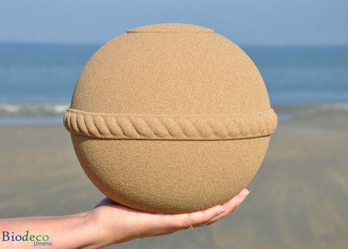 De Sand Round zee-urn in de hand, op het strand van Scheveningen met de Noordzee op de achtergrond